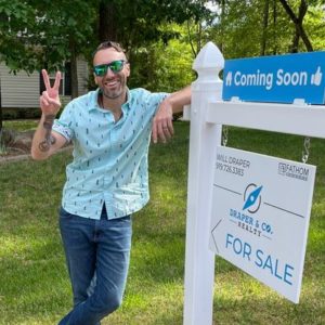 Will Draper Standing beside Fathom Realty For Sale Real Estate Sign