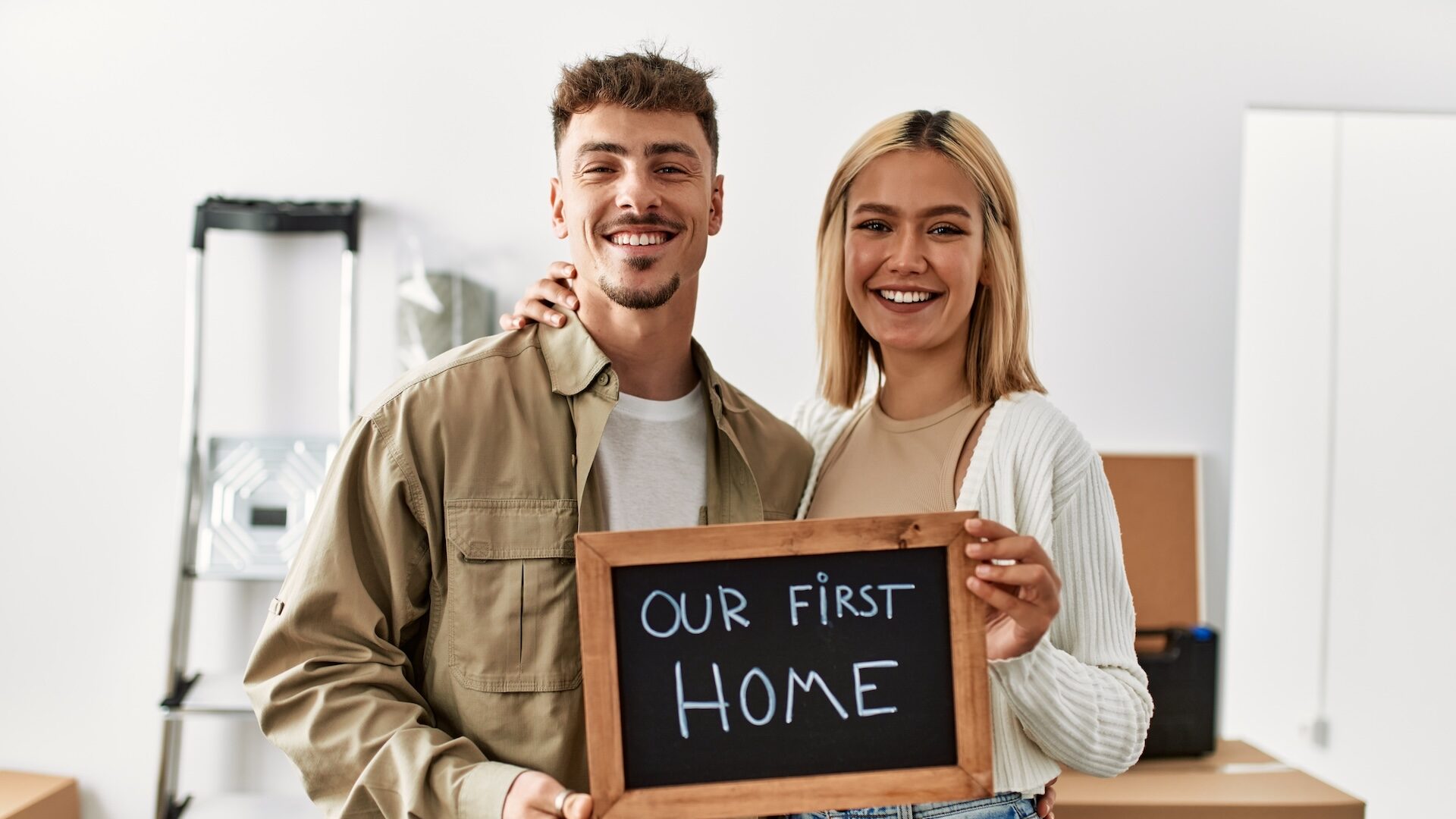 Young caucasian couple smiling happy holding blackboard with our first home message at their new starter home.